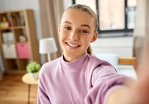 A young girl is taking a selfie with a smile in a bedroom.