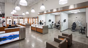 An inside look at a Costco Optical store, featuring a reception desk, chairs, and medical equipment in a glass-walled examination room.