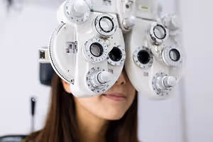 A woman with glasses is looking through a device with lenses and dials that has a white background