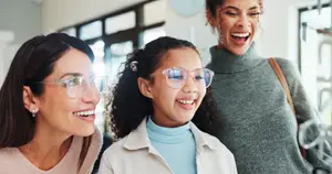 Three women smiling at each other in a store, one wearing glasses and the other wearing sunglasses