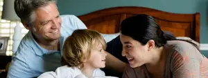 A family of three people sitting in bed and smiling at each other