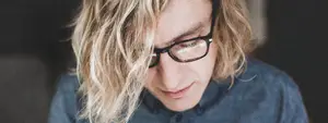 A man with glasses and blonde hair is looking at something in front of him