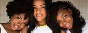 Three African American women smiling and posing for a photo, one of them wearing a yellow necklace