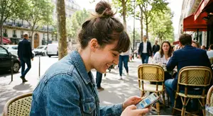 A woman sits on a chair in a cafe, using her phone, with people walking by on the street behind her.