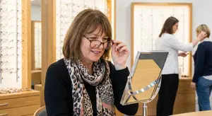 A woman wearing glasses is smiling and looking in a mirror in a store