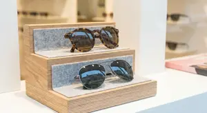 Two pairs of sunglasses on a wooden display stand with gray felt lining on a white countertop