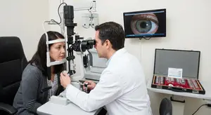 A doctor is examining a woman's eyes with a slit lamp in an examination room.