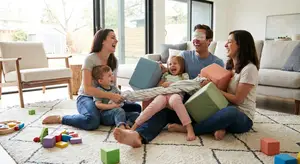 A family with two parents, two children, and a baby are sitting on the floor in a living room, laughing and playing with toys.