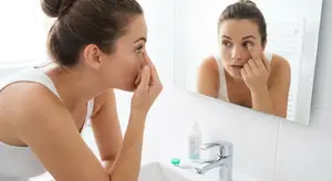 Woman applying eye drops in front of a bathroom mirror