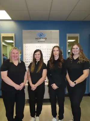 Four women in black outfits stand in front of a blue wall, likely posing for a photo.