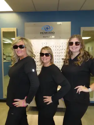 Three women in black uniforms pose for a photo in front of a sign for Howard Family Eye Care.
