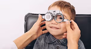 A child wearing glasses is being examined by a doctor or optometrist