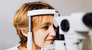 A woman looking through a slit lamp while wearing glasses and smiling