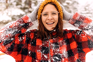 Woman smiling and posing in the snow wearing a red and black plaid coat and yellow hat.