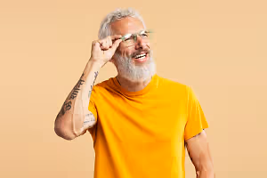 An older man with a beard is smiling and adjusting his glasses.