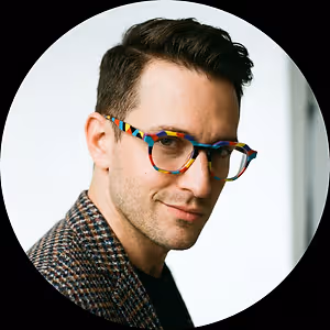 A smiling man wearing colorful glasses and a patterned jacket