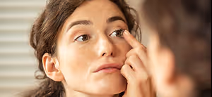 woman putting in a contact lens in front of a mirror