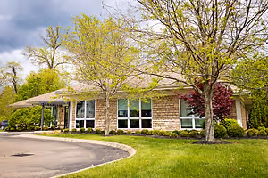 A house with glass windows, a driveway, and lush green grass under a cloudy sky.