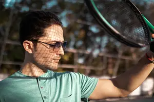 A man wearing a green polo shirt and sunglasses holding a tennis racket in his hand. He seems to be posing for a photograph