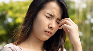 A woman with her eyes closed holding her temple