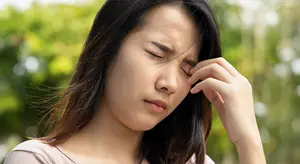 A woman with her eyes closed holding her temple