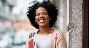 African American woman holding books and smiling in a city setting