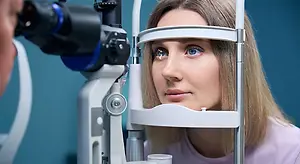 A woman is looking into a phoropter while a doctor examines her eyes