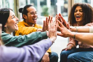 A group of people sitting in a room, smiling, and giving high fives to each other.