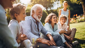 A group of family members sitting on the grass in the garden, with a man in the middle laughing and the others smiling at him