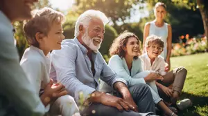 A group of family members sitting on the grass in the garden, with a man in the middle laughing and the others smiling at him