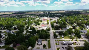 Aerial view of a town with many buildings, trees, and a wide road in the middle, under a partly cloudy sky.