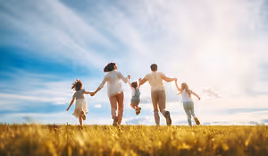 A group of people are running in a grassy field under a cloudy sky, some holding hands.