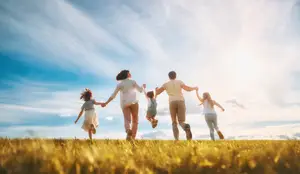 A group of people are running in a grassy field under a cloudy sky, some holding hands.