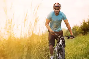 A man riding a bicycle in a field with tall grass and bushes.