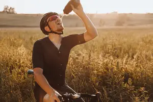 A man is riding a bicycle and drinking water in a grassy field during the day