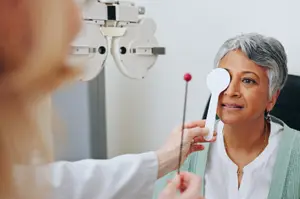An older woman getting her eye examined by a doctor with a white eye chart in the background.