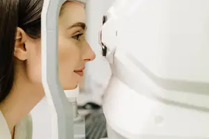 A woman is examining her eyes through a device resembling a robot in an eye clinic.