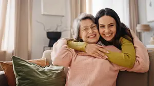 Two women hugging on a couch with pillows and a lamp in the background