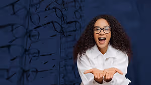 A smiling woman in glasses stands in front of a wall of glasses.