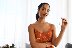 A woman wearing an orange polka-dot dress and holding a pair of glasses