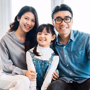 A family of three sitting together, smiling, and posing for a picture in a room with white walls and curtains.