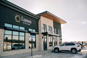 A white SUV is parked in front of the Lumen Eyecare building.