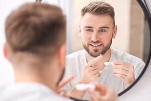 A man with a beard looking at himself in a mirror while cleaning his teeth with a toothbrush