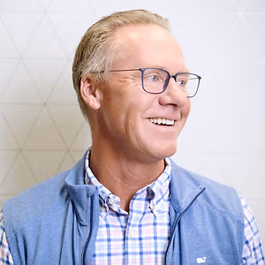 Close up of smiling man with short hair wearing glasses and a navy vest and plaid shirt