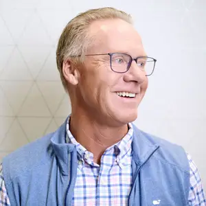Close up of smiling man with short hair wearing glasses and a navy vest and plaid shirt