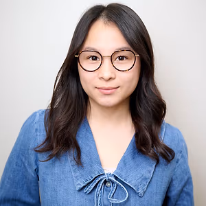 A woman wearing glasses and a denim shirt is smiling at the camera