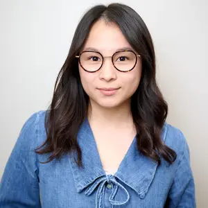 A woman wearing glasses and a denim shirt is smiling at the camera