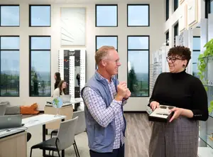 A man and a woman are smiling and looking at a box of glasses in a modern office.