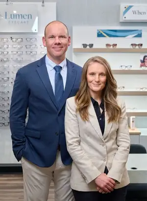 A man and a woman standing next to each other in front of an optician's shop