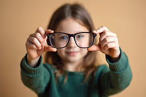 A young girl with glasses holding a pair of glasses